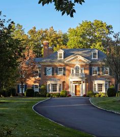 a large brick house with lots of windows and trees in the front yard, surrounded by lush green grass