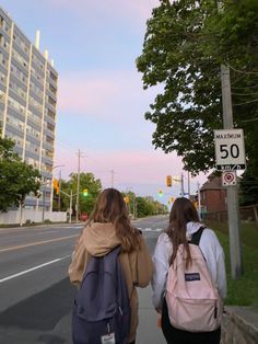 two girls walking down the street with backpacks on