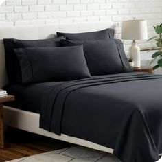 a bed with black sheets and pillows in a room next to a white brick wall