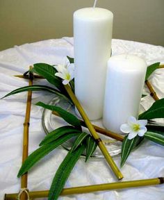 two white candles sitting on top of a table next to some bamboo sticks and flowers