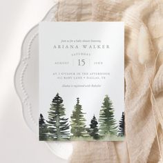 a watercolor pine tree wedding card on top of a white plate next to a piece of cloth