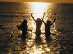 three people standing in the water with their arms up and hands raised above their heads