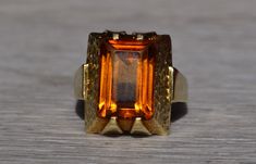 The Whitsett: Ladies Mid Century Citrine Cocktail Ring in 14K Yellow Gold. Crafted in 14 karat white gold is this mid century style statement ring. Set in the center of this ring is a 13mm x 9mm emerald cut citrine. The ring is stamped Germany and is currently a finger size 7.5 yet can be adjusted in size for an additional charge upon request. Love this piece, but don't have the money to spend right now?  We offer FREE layaway on every item in our shop.  With just 20% down, take one full year (i Retro Polished Rings For Formal Events, Retro Formal Rings With Polished Finish, Retro Rings With Polished Finish For Formal Occasions, Modern Formal Hallmarked Topaz Ring, Retro Orange Jewelry For Formal Events, Retro Orange Jewelry For Formal Occasions, Vintage Orange Rings For Formal Occasions, Orange Vintage Rings For Formal Occasions, Retro 14k Gold Formal Rings