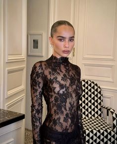 a woman standing in front of a black and white chair wearing a sheer lace top