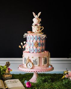 a three tiered cake decorated in pink, blue and white with rabbit figurines on top