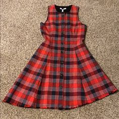 a red and black plaid dress sitting on top of a carpeted floor next to a wall