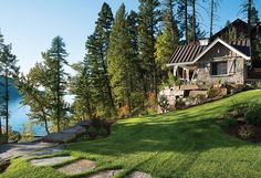 a house on the side of a hill with trees and water in the back ground