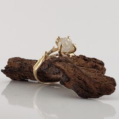 a gold ring sitting on top of a piece of driftwood with a white diamond