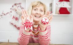 a woman in red and white sweater holding her hands up with christmas decorations on the wall behind her