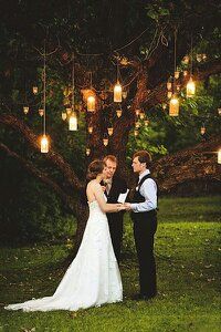 a bride and groom standing in front of a tree with lanterns hanging from the branches