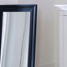 a black framed mirror sitting next to a white dresser