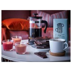 three candles are sitting on a table next to two cups and a coffee pot with some chocolate in it