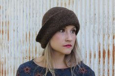 a woman wearing a brown hat standing in front of a rusted metal wall and looking off to the side