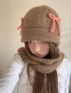 a young woman wearing a knitted hat and scarf with an orange bow on it