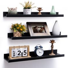 two black shelves with pictures, flowers and an alarm clock on each shelf in front of a white wall