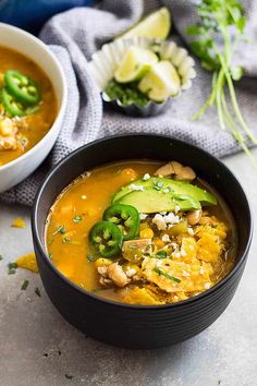 a black bowl filled with soup and topped with green peppers, avocado and cheese