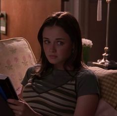 a woman sitting on a couch holding a book and looking at the camera while reading it