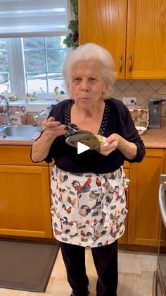 an older woman standing in a kitchen holding a plate with food on it and looking at the camera