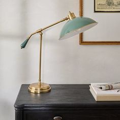 a desk lamp sitting on top of a black dresser next to a framed picture and newspaper