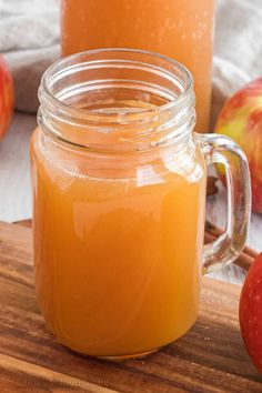 two jars filled with apple cider sitting on top of a wooden cutting board next to apples