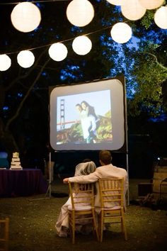 two people sitting at a table watching a movie on the screen in front of them