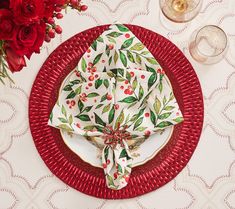 a place setting with red flowers and napkins on it, along with wine glasses