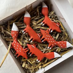 four red and white wooden toy animals in a cardboard box with straw on the floor