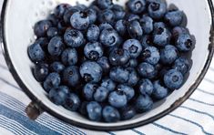 blueberries are in a glass bowl on a tablecloth with a cloth behind it