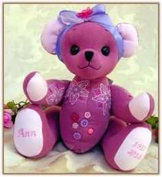 a pink teddy bear sitting on top of a white tablecloth with flowers in the background