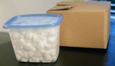 a plastic container filled with white balls sitting on top of a table next to a cardboard box