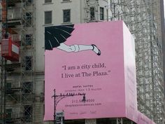 a large pink billboard on the side of a tall building with scaffolding around it that says i am a city child, i live at the plaza