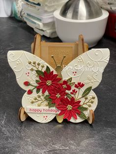 a white butterfly with red flowers on it's wings sitting on a counter top