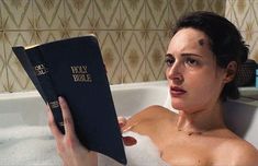 a woman in a bathtub holding a bible next to her face and looking at the camera