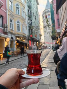 a person holding a cup with red liquid in it on a white plate and people walking down the street