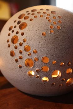 a vase with holes on it sitting on top of a wooden table next to a cell phone