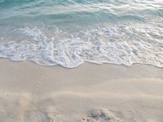 the ocean waves are coming in to the sandy beach with white foamy sand and blue water