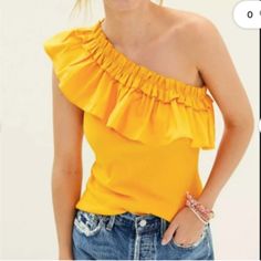 a woman wearing a yellow top with ruffles on it's shoulders and her hands in her pockets