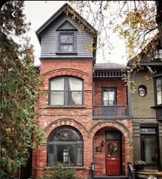 an old brick house with a red door and window on the second floor is surrounded by trees