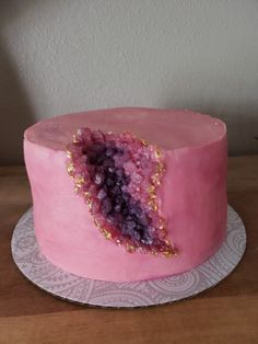 a pink cake with gold sprinkles is on a white doily and sits on a wooden table