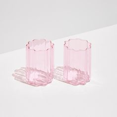 two pink glass vases sitting on top of a white table next to each other