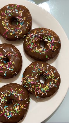 six donuts with chocolate frosting and sprinkles on a white plate