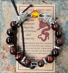 "Introducing the GOOD LIFE/GOOD VIBES bracelet! A bracelet that is beautiful and meaningful.    SYMBOLIC MEANING OF THIS BRACELET: 🔥 Dragons are symbols of prosperity, success and good luck.   The positive energy from this bracelet helps you LIVE YOUR BEST LIFE! This POWERFUL bracelet:   👍 Features SiLVER dragon head beads, 👍 🔥 FIRE DRAGON (red & yellow central bead) or 🧊 ICE DRAGON (clear central bead), 👍 Has 10mm Red Tiger's Eye Beads interspersed with grey Hematite spacer Beads, 👍 Is m Nickel-free Brown Bracelets As Gift, Nickel-free Brown Bracelets For Gifts, Spiritual Round Braided Bracelets As Gifts, Spiritual Round Braided Bracelet As Gift, Spiritual Braided Bracelets As A Gift, Spiritual Braided Bracelet Gift, Spiritual Round Amber Bracelet, Meaningful Round Bead Bracelets As Gift, Meaningful Round Beads Bracelets As Gift