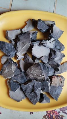 a yellow plate filled with chunks of gray rocks on top of a tiled countertop