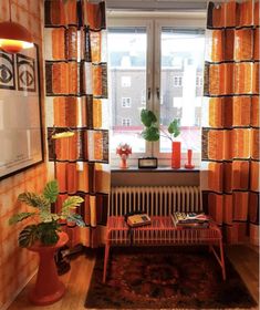 a living room filled with furniture and orange curtains on the window sill next to a radiator