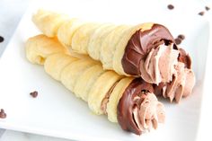 three chocolate covered desserts on a white plate with chocolate chips scattered around the edges