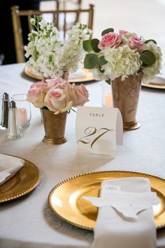 the table is set with place cards and flowers in gold vases, along with napkins