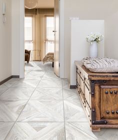 a room with white walls and flooring that looks like herringbone tiles, has a wooden trunk on it