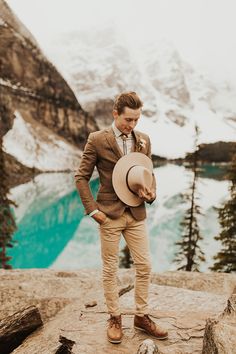 a man in a suit and hat standing on top of a mountain looking at the water