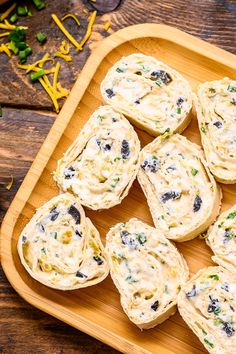 a wooden tray filled with rolls covered in cheese and olives on top of a table