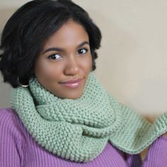 a woman with black hair wearing a green scarf and purple sweater looking at the camera